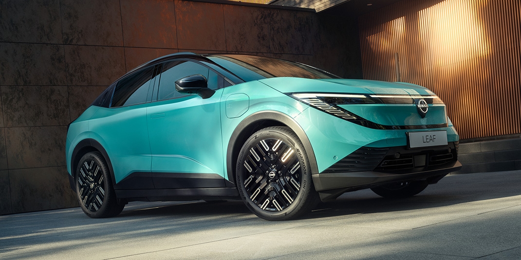 Nissan LEAF in Luminous Teal, Frontansicht schräg, modernes Design mit LED-Scheinwerfern, vor einer Holzwand.